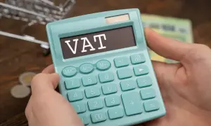 Kalkulator z napisem VAT w rękach, symbolizujący zwolnienie podmiotowe z VAT. W tle monety i banknoty.