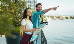 Para młodych turystów z mapą i aparatem planuje tani city break, wskazując kierunek zwiedzania.