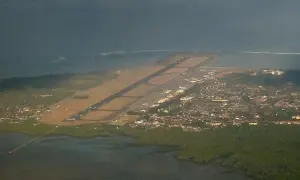 Widok z lotu ptaka na lotnisko na Bali, z pasem startowym biegnącym wzdłuż wybrzeża i miastem w tle.