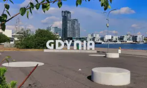 Napis "GDYNIA" na tle nowoczesnych budynków i portu.