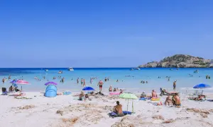 Słoneczna plaża Cala Agulla tętni życiem. Ludzie kąpią się w krystalicznie czystej wodzie, opalają na piasku i odpoczywają pod parasolami.