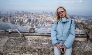Kobieta w jasnoniebieskiej kurtce i okularach przeciwsłonecznych na tle panoramy Stambułu.