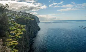 Widok na klif z domkami na zboczu i oceanem. Zastanawiasz się, ile się leci na Maderę, patrząc na ten krajobraz?