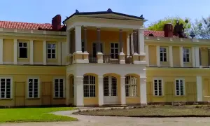 Pałac w Waplewie z kolumnowym portykiem i żółtą fasadą, otoczony zielenią.