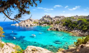 Turkusowa woda zatoki na Costa Smeralda, łodzie kołyszące się na falach, skaliste wybrzeże porośnięte zielenią.