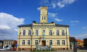 Żółty budynek ratusza z wieżą zegarową i flagą na tle błękitnego nieba.