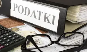 Segregator z napisem "PODATKI", okulary, kalkulator i pieniądze na dokumentach. Czas na rozliczenie PIT-2.