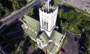 Widok z lotu ptaka na białą wieżę kościoła z zielonym dachem i otaczającą go drogę z samochodami.