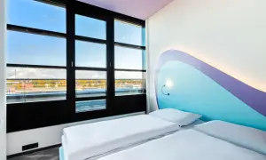 Pokój z dwoma łóżkami w **Radisson Blu Hotel Rostock**. Duże okno z widokiem na miasto i wodę. Nowoczesne, jasne wnętrze z kolorowym zagłówkiem.