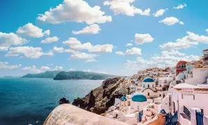 Santorini, Grecja. Białe domki z niebieskimi kopułami na klifie nad morzem. Idealne miejsce na wakacje, zastanawiasz się, ile się leci do Grecji?