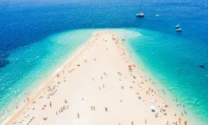 Złoty róg Chorwacja, plaża z turkusową wodą i ludźmi odpoczywającymi na piasku. W oddali widać łodzie.
