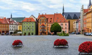 Kolorowy rynek w Chebie z kamienną nawierzchnią i ozdobnymi donicami z czerwonymi kwiatami.