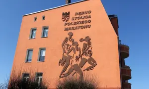 Pomarańczowa ściana budynku z płaskorzeźbą biegaczy i napisem "DĘBNO STOLICA POLSKIEGO MARATONU".