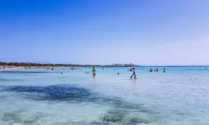 Słoneczny dzień na plaży Es Trenc. Ludzie kąpią się w krystalicznie czystej wodzie, ciesząc się wakacjami.