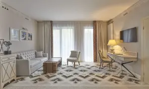 Elegancki pokój hotelowy z sofą, fotelem i biurkiem. Wnętrze w stylu 4-gwiazdkowym, z dywanem o geometrycznym wzorze.