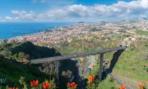 Widok na Funchal, Maderę, z autostradą przecinającą dolinę i wpadającą do tuneli. W oddali widać ocean i port.