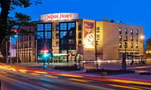 Hotel Qubus Gorzów nocą, z widocznymi światłami samochodów na ulicy i neonem hotelu.