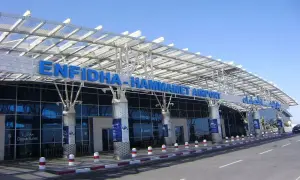 Nowoczesny budynek lotniska Enfidha-Hammamet w Tunezji, z niebieskimi literami nazwy i przeszkloną fasadą.