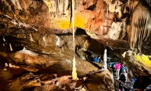 Wnętrze jaskini Macochy, z naciekami i stalagmitami. Grupa turystów schodzi po schodach, podziwiając podziemne piękno.