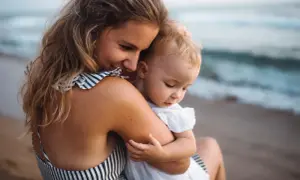 Ciepłe objęcia mamy i dziecka na plaży. Cudowne wakacje z niemowlakiem nad morzem.