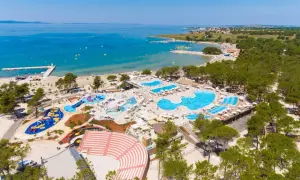 Widok z lotu ptaka na kompleks basenów i plażę z turystami w słoneczny dzień.