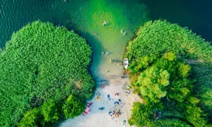 Letnie orzeźwienie nad jednym z najpiękniejszych jezior w Polsce. Ludzie kąpią się, plażują, a łódka czeka przy brzegu.