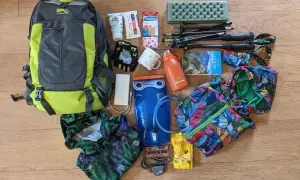 Plecak, kijki trekkingowe, bidon, apteczka i inne akcesoria turystyczne ułożone na drewnianym tle.