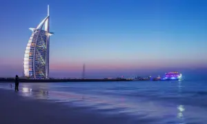 Wieżowiec Burdż al-Arab i oświetlony statek na tle nocnego nieba nad Zatoką Perską.