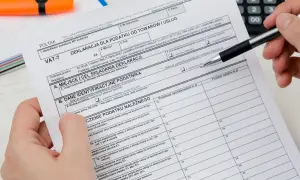 Dłoń z długopisem wypełnia deklarację VAT-7, dokument podatkowy z polami do wpisania danych.