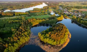 Widok z lotu ptaka na jezioro otoczone lasem i małą wioskę na Mazurach.