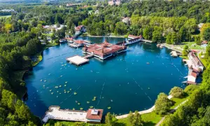 Malownicze jezioro Balaton z termalnymi basenami i otaczającym je lasem. Ludzie pływają i relaksują się w wodzie.