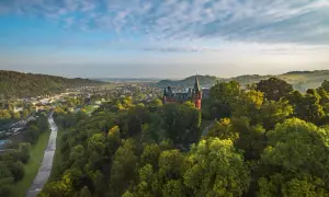 Widok na zamek w Hradcu nad Moravicí otoczony zielonymi drzewami, z miastem i rzeką w tle.
