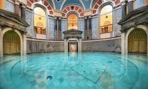 Wnętrze zabytkowego **zdroju** z basenem o turkusowej wodzie, ozdobnymi kolumnami i łukowymi oknami.