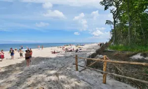 Słoneczny dzień na plaży w Karwieńskich Błotach. Ludzie odpoczywają na piasku, a morze spokojnie faluje.
