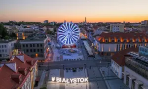 Widok z góry na plac z podświetlanym napisem #BIAŁYSTOK i diabelskim młynem o zachodzie słońca.