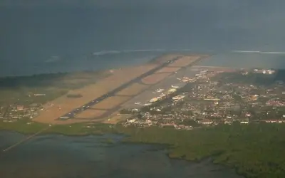 Widok z lotu ptaka na lotnisko na Bali, z pasem startowym biegnącym wzdłuż wybrzeża i miastem w tle.