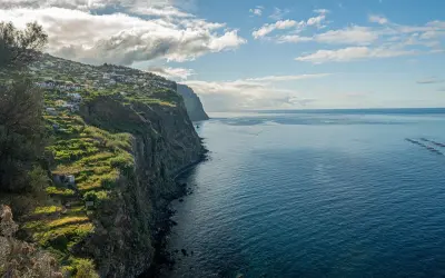 Widok na klif z domkami na zboczu i oceanem. Zastanawiasz się, ile się leci na Maderę, patrząc na ten krajobraz?