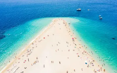 Złoty róg Chorwacja, plaża z turkusową wodą i ludźmi odpoczywającymi na piasku. W oddali widać łodzie.