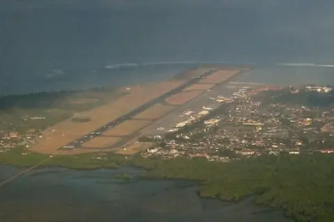 Widok z lotu ptaka na lotnisko na Bali, z pasem startowym biegnącym wzdłuż wybrzeża i miastem w tle.