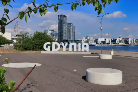Napis "GDYNIA" na tle nowoczesnych budynków i portu.