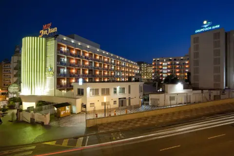 Hotel Don Juan Resort nocą, z neonowym oświetleniem i widokiem na wiele balkonów.
