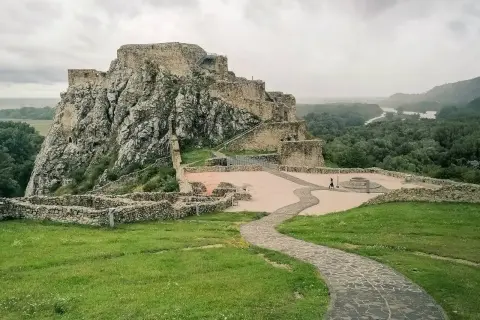 Ruiny zamku Devín na skalistym wzgórzu nad Dunajem, z kamienną ścieżką i zielonymi trawnikami.