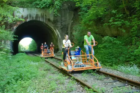 Rodzina na drezynach w Bieszczadach pokonuje malowniczy tunel kolejowy, ciesząc się zielenią i aktywnym wypoczynkiem.