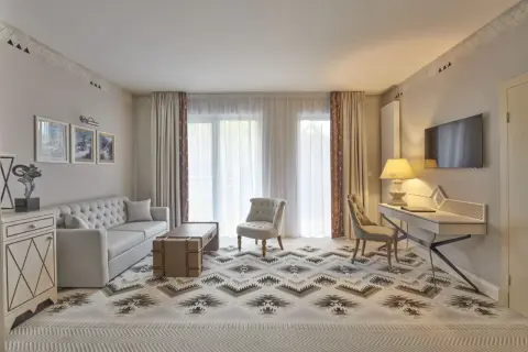 Elegancki pokój hotelowy z sofą, fotelem i biurkiem. Wnętrze w stylu 4-gwiazdkowym, z dywanem o geometrycznym wzorze.
