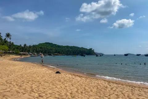 Piękna plaża i turkusowe morze, idealne na wietnam wakacje. W oddali widać łodzie i zieloną wyspę.