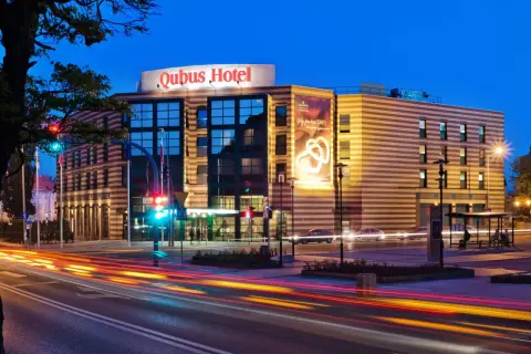 Hotel Qubus Gorzów nocą, z widocznymi światłami samochodów na ulicy i neonem hotelu.