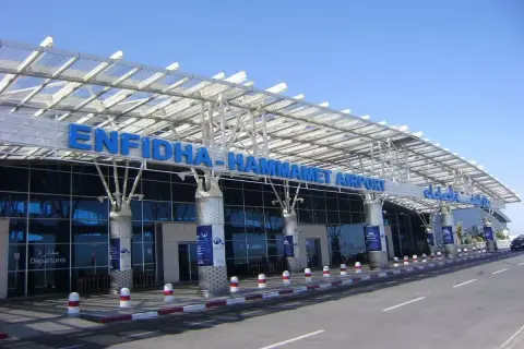 Nowoczesny budynek lotniska Enfidha-Hammamet w Tunezji, z niebieskimi literami nazwy i przeszkloną fasadą.