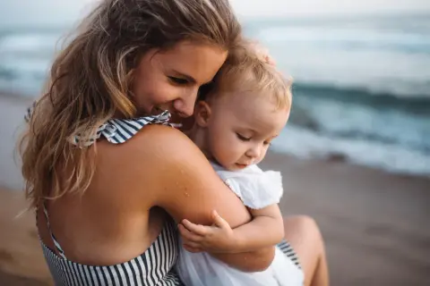 Ciepłe objęcia mamy i dziecka na plaży. Cudowne wakacje z niemowlakiem nad morzem.