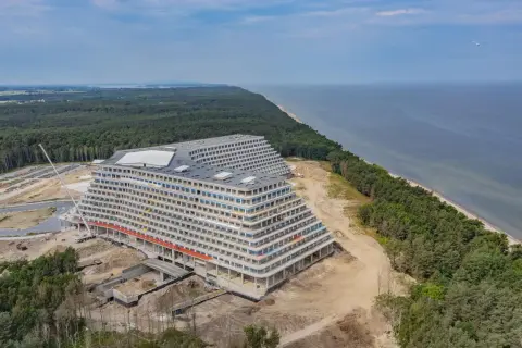 Ogromny hotel w kształcie tarasów w budowie, nad morzem, otoczony lasem.