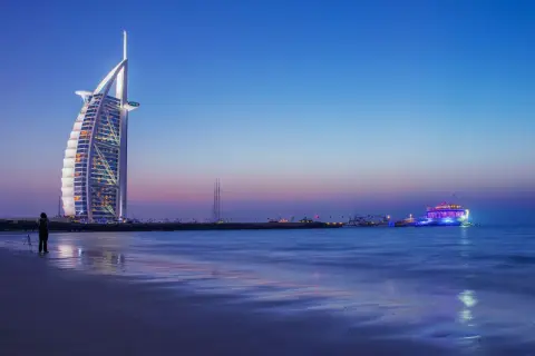 Wieżowiec Burdż al-Arab i oświetlony statek na tle nocnego nieba nad Zatoką Perską.